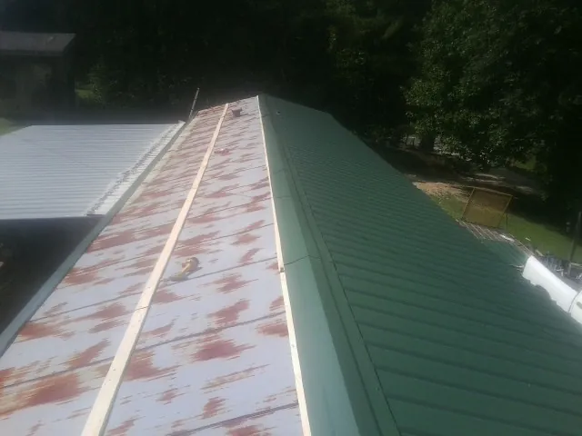 Old rusted panels beside newly installed green metal roofing — Wind Damage Roof Repair by Roofing Brothers in Holden