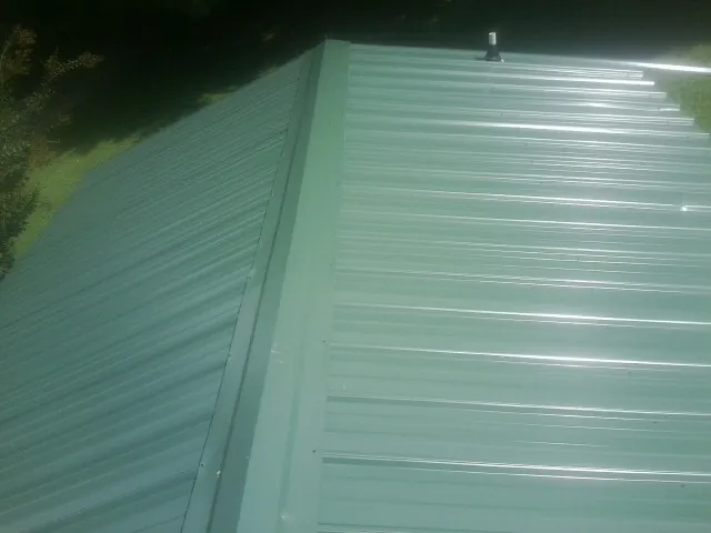 New green metal panels meeting at the ridge of a roof — Flat Roof Repair work by our crew in Holden