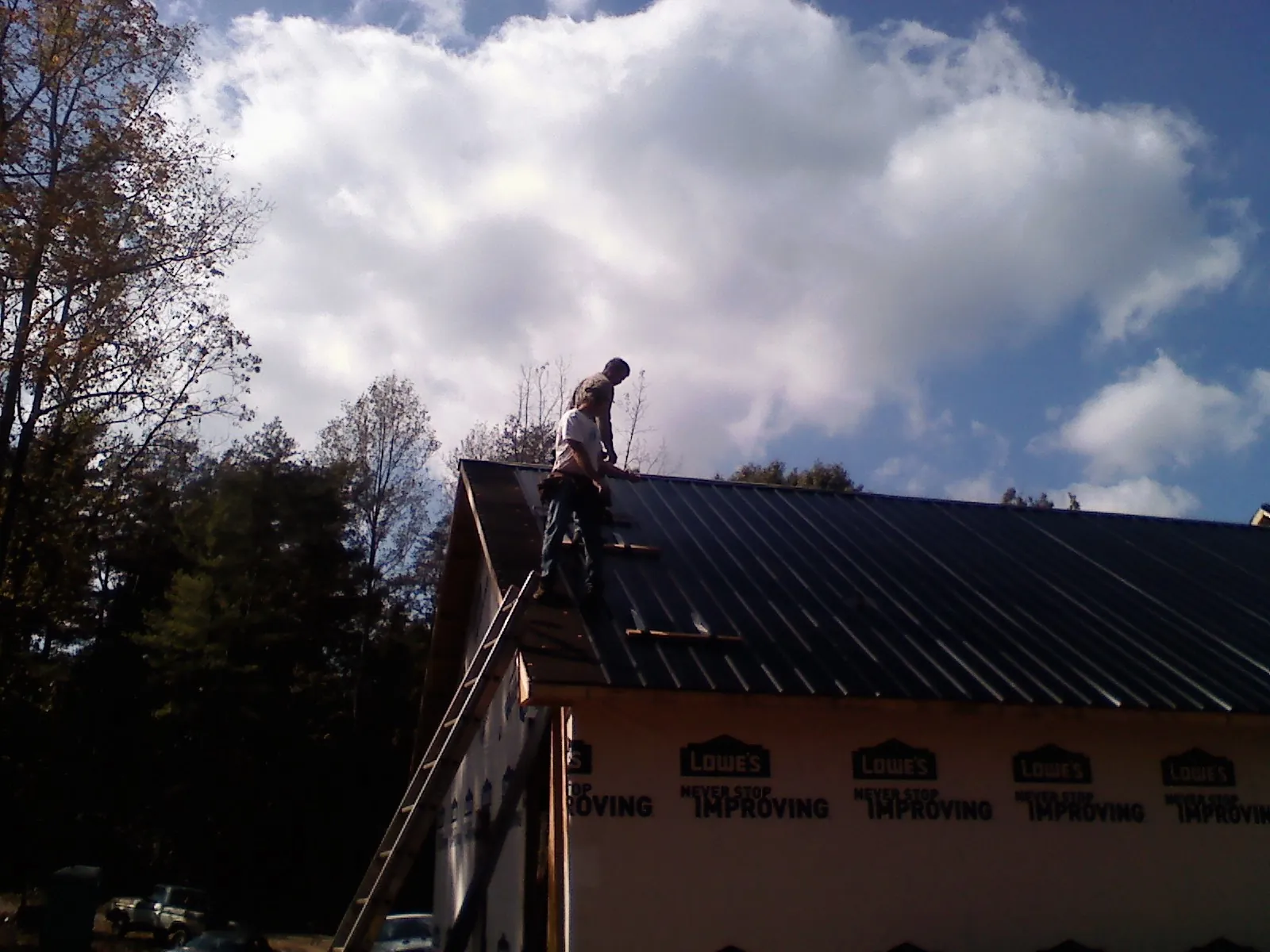 Roofer fastening dark metal panels high against a cloudy sky, from a Roof Inspection job in Holden